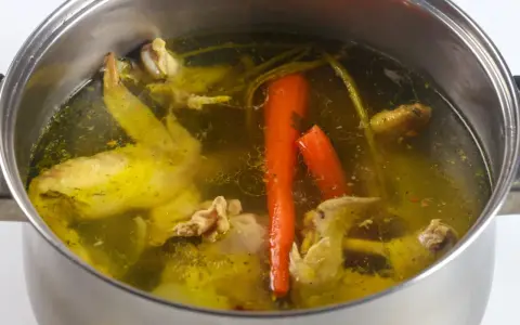 Gotowanie rosołu pod przykryciem to sekret głębokiego smaku. W garnku bulgocze złocisty płyn z kawałkami kurczaka i marchewką.