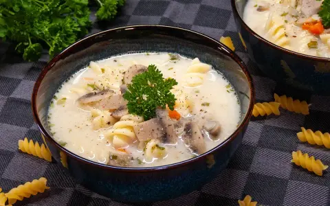 Aksamitna zupa pieczarkowa z makaronem, udekorowana natką pietruszki. Na stole leżą spiralne fusilli, zachęcając do spróbowania.