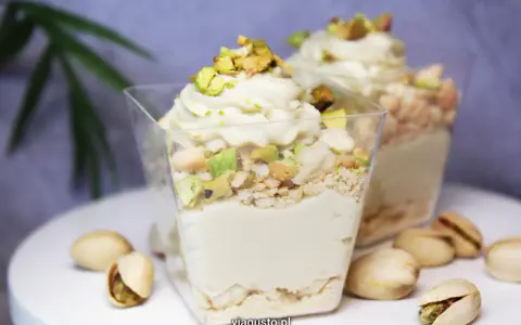 Pyszny deser w pucharku z kremową masą pistacjową, posypany kawałkami pistacji i okruszkami.