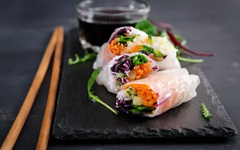 Świeże spring rolls z warzywami i łososiem, podane z sosem.