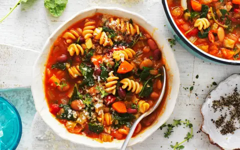 Minestrone co to? Aromatyczna zupa z makaronem, fasolą, warzywami i ziołami, podana w białej misce.