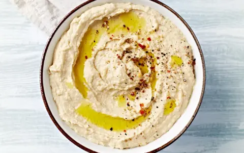 Kremowy hummus polany oliwą, posypany pieprzem i papryką. Idealny do pieczywa, jako dodatek do dań. Prosty hummus przepis.