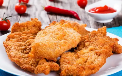 Chrupiące kotlety z kurczaka na talerzu, obok pomidorki i ketchupu. Idealne, gdy zastanawiasz się, ile smażyć kurczaka.