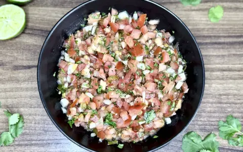 Świeże, posiekane pomidory, cebula, kolendra i papryczka jalapeno tworzą apetyczne pico de gallo w czarnej misce.