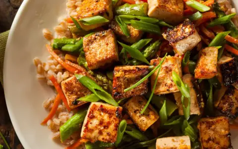 Pyszne tofu na obiad z ryżem, szparagami i marchewką. Danie wygląda apetycznie i zdrowo.
