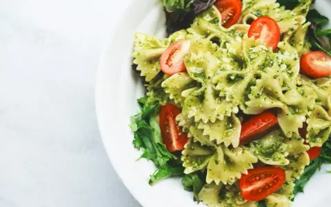 Pyszny makaron z pesto, udekorowany pomidorkami koktajlowymi i świeżą sałatą, podany na białym talerzu.