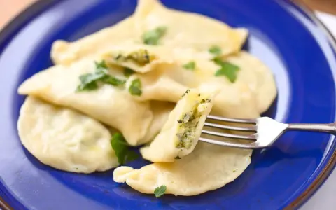 Pyszne pierogi ze szpinakiem i serem, udekorowane natką pietruszki, czekają na widelcu.