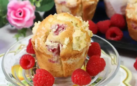 Pyszne muffinki z malinami, posypane kruszonką, otoczone świeżymi malinami. Idealne na deser.