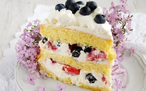Pyszny tort z bitą śmietaną i mascarpone, przełożony owocami leśnymi, ozdobiony jagodami i kwitnącym bzem.