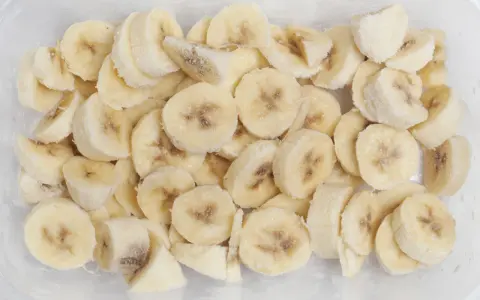 Pokrojone w plasterki banany w pojemniku, pokryte szronem. Tak, banany można mrozić, idealne do smoothie!