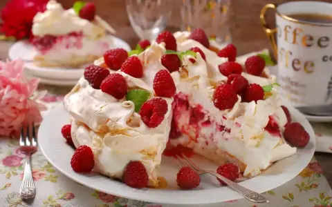 Pyszny tort bezowy z malinami, udekorowany listkami mięty. Idealny deser na letnie popołudnie.