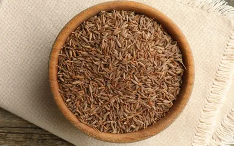 Drewniana miseczka pełna nasion kminu, znanego też jako kumin. Aromatyczna przyprawa na lnianej serwetce.