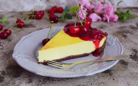 Sernik z polewą z frużeliny wiśniowej i świeżymi wiśniami na talerzu, gotowy do degustacji.