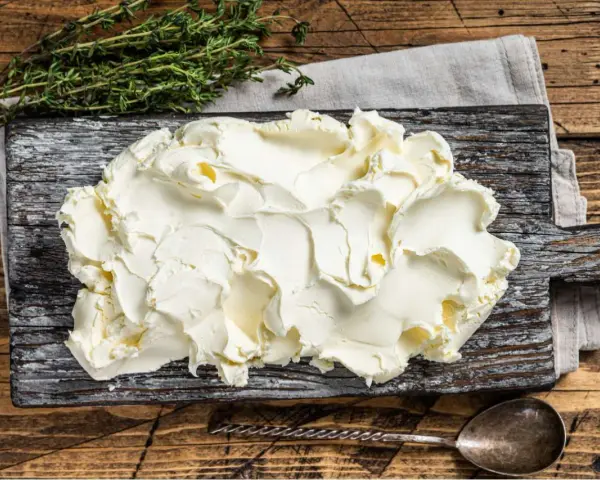 Kremowe mascarpone na desce, obok gałązka tymianku. Czy mascarpone można mrozić? Tak, ale po rozmrożeniu może stracić idealną konsystencję.