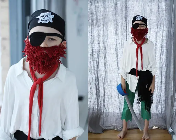 Dziecko w stroju pirata: czarna bandama z czaszką, opaska na oko, czerwona broda z włóczki, biała koszula, zielone spodnie. Jak zrobić strój pirata samemu.