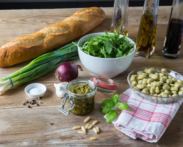 Składniki na pyszne pesto z bobu: świeży bób, bazylia, orzeszki piniowe, czosnek, oliwa, bagietka i rukola.