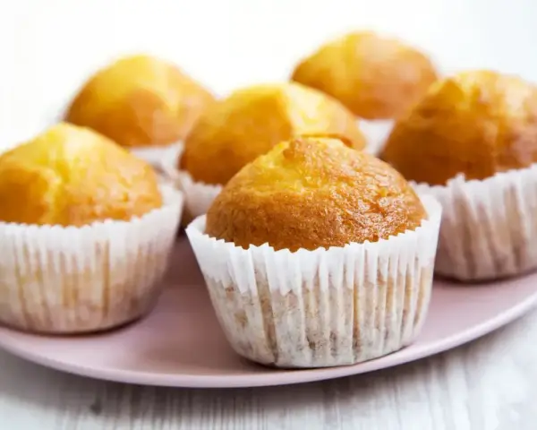 Idealny przepis na wilgotne i puszyste muffinki. Złociste, pachnące babeczki na różowym talerzyku.