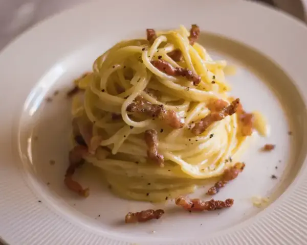 Pyszna carbonara bez śmietany, z chrupiącym boczkiem i czarnym pieprzem, podana na białym talerzu.