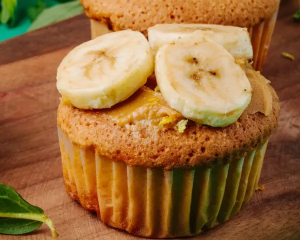 Pyszne muffinki bananowe z kremem orzechowym i plasterkami banana na drewnianej desce.