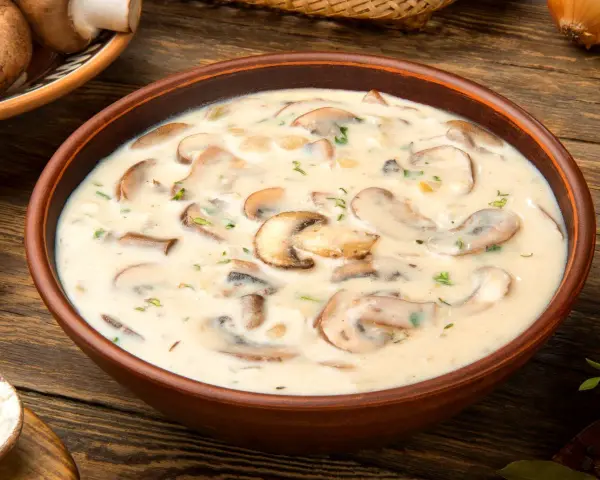 Aksamitna zupa pieczarkowa w glinianej misce, pełna kawałków pieczarek i ziół, na drewnianym stole.