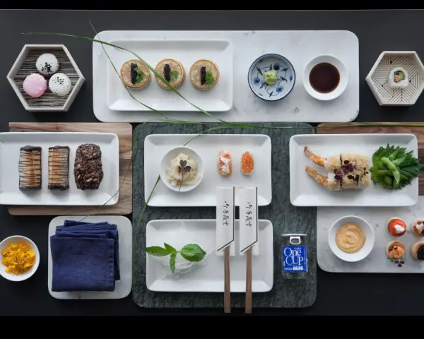 Elegancka aranżacja stołu z różnorodnymi przekąskami, w tym mini naleśnikami z kawiorem, sushi, krewetkami w tempurze i makaronikami. Idealne na wieczór, gdy masz ochotę na coś pysznego do sushi.