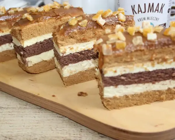 Pyszne ciasto z kajmakiem, przełożone kremem i biszkoptem, ozdobione kandyzowanymi skórkami.