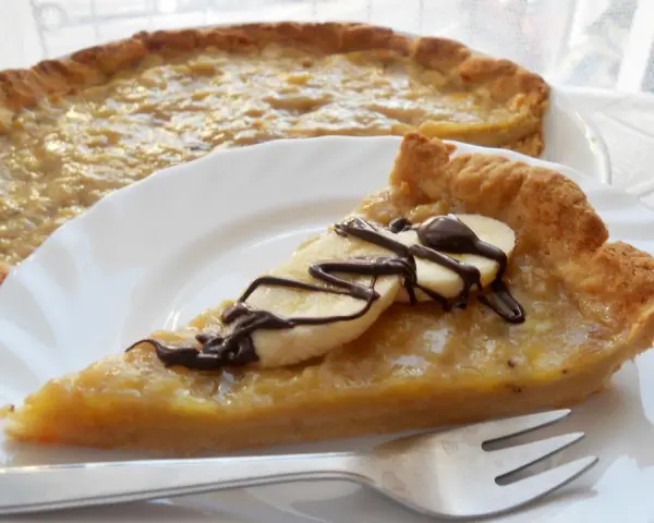 Pyszna tarta z bananami, udekorowana czekoladą i plasterkami banana, czeka na talerzu.