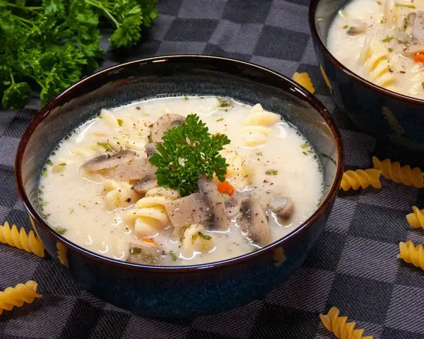 Aksamitna zupa pieczarkowa z makaronem, udekorowana natką pietruszki. Na stole leżą spiralne fusilli, zachęcając do spróbowania.