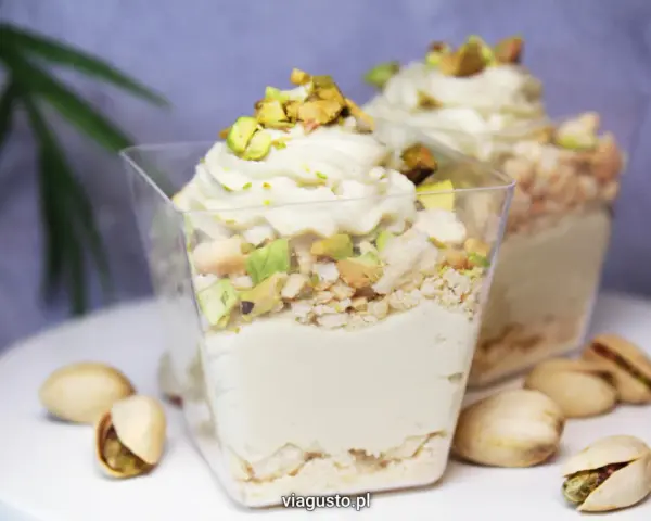 Pyszny deser w pucharku z kremową masą pistacjową, posypany kawałkami pistacji i okruszkami.