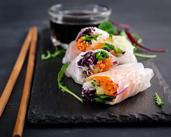 Świeże spring rolls z warzywami i łososiem, podane z sosem.