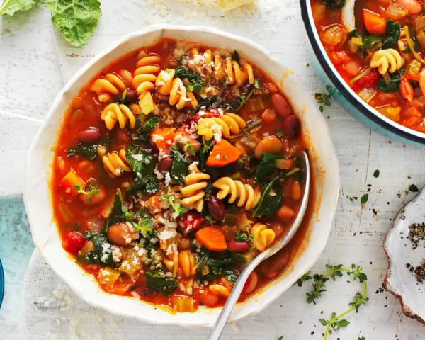 Minestrone co to? Aromatyczna zupa z makaronem, fasolą, warzywami i ziołami, podana w białej misce.