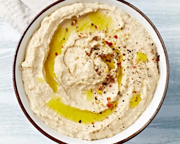 Kremowy hummus polany oliwą, posypany pieprzem i papryką. Idealny do pieczywa, jako dodatek do dań. Prosty hummus przepis.