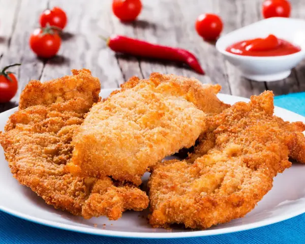 Chrupiące kotlety z kurczaka na talerzu, obok pomidorki i ketchupu. Idealne, gdy zastanawiasz się, ile smażyć kurczaka.