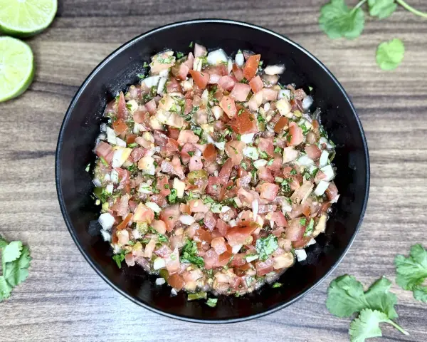 Świeże, posiekane pomidory, cebula, kolendra i papryczka jalapeno tworzą apetyczne pico de gallo w czarnej misce.