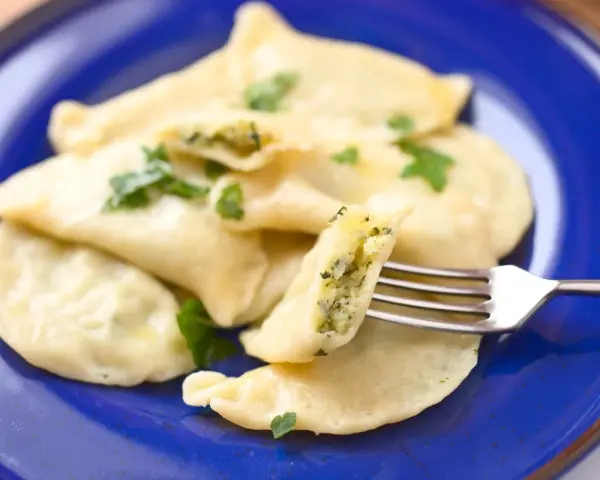 Pyszne pierogi ze szpinakiem i serem, udekorowane natką pietruszki, czekają na widelcu.