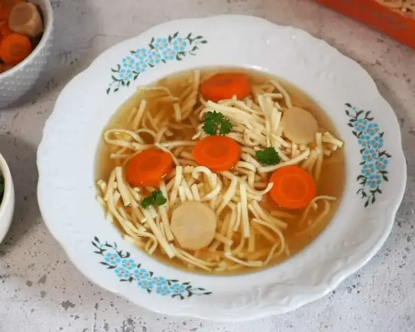Aksamitny rosół z kaczki z makaronem nitki, marchewką i kawałkami mięsa, ozdobiony natką pietruszki.