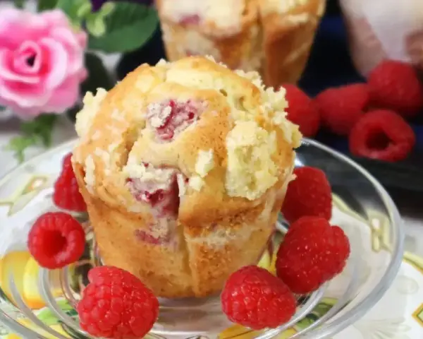 Pyszne muffinki z malinami, posypane kruszonką, otoczone świeżymi malinami. Idealne na deser.
