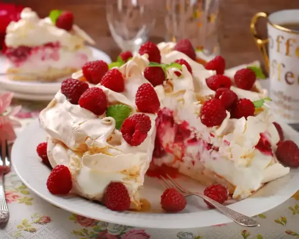 Pyszny tort bezowy z malinami, udekorowany listkami mięty. Idealny deser na letnie popołudnie.