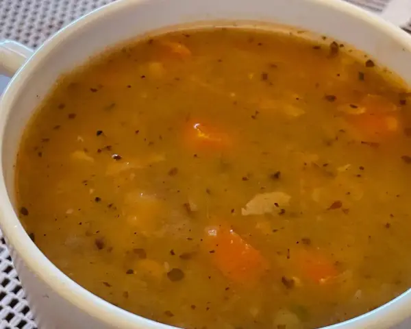 Gęsta, aromatyczna zupa grochowa z kawałkami marchewki i przyprawami, podana w białej miseczce.