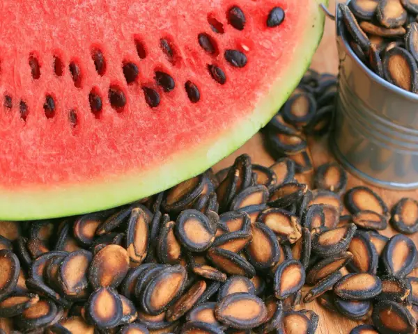 Kawałek arbuza i wiaderko pełne prażonych pestek. Czy można jeść pestki arbuza? Tak, są smaczną przekąską!