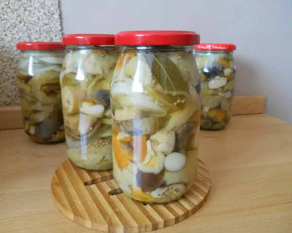 Słoiki z grzybami marynowanymi, pełne aromatycznych przypraw i kawałków grzybów, gotowe do zimowych przetworów.