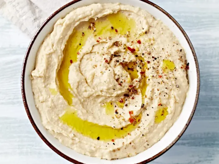 Kremowy hummus polany oliwą, posypany pieprzem i papryką. Idealny do pieczywa, jako dodatek do dań. Prosty hummus przepis.