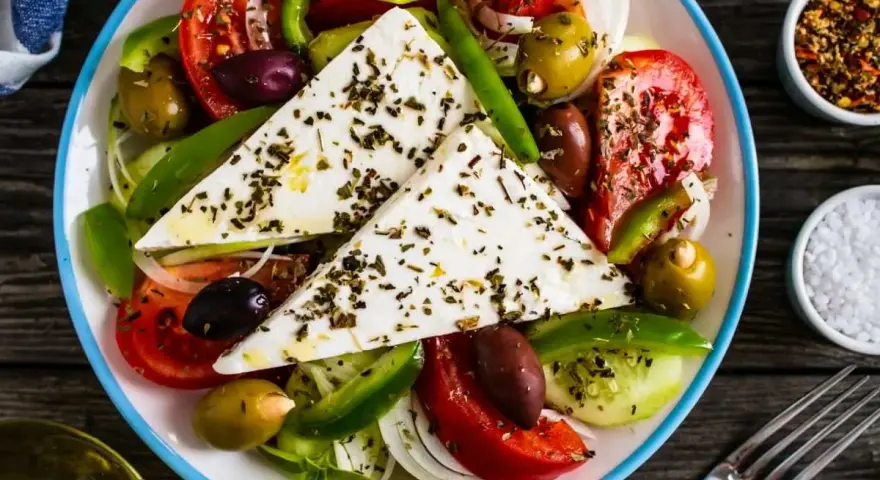 Kolorowa sałatka z fetą, pomidorami, ogórkiem, papryką i oliwkami, posypana ziołami.