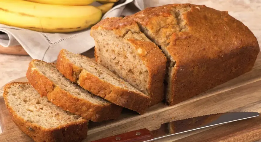 Pyszny, domowy chlebek bananowy, pokrojony na kromki, leży obok dojrzałych bananów.