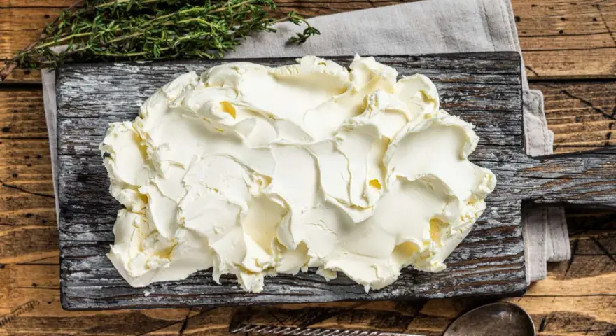 Kremowe mascarpone na desce, obok gałązka tymianku. Czy mascarpone można mrozić? Tak, ale po rozmrożeniu może stracić idealną konsystencję.