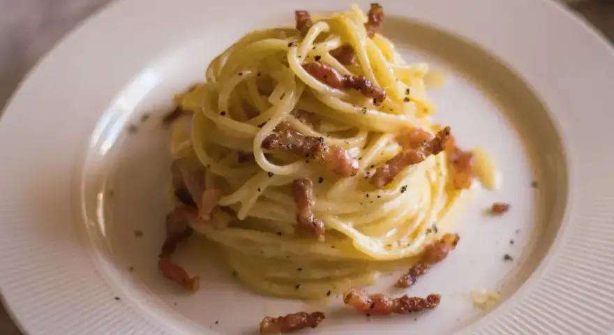 Pyszna carbonara bez śmietany, z chrupiącym boczkiem i czarnym pieprzem, podana na białym talerzu.
