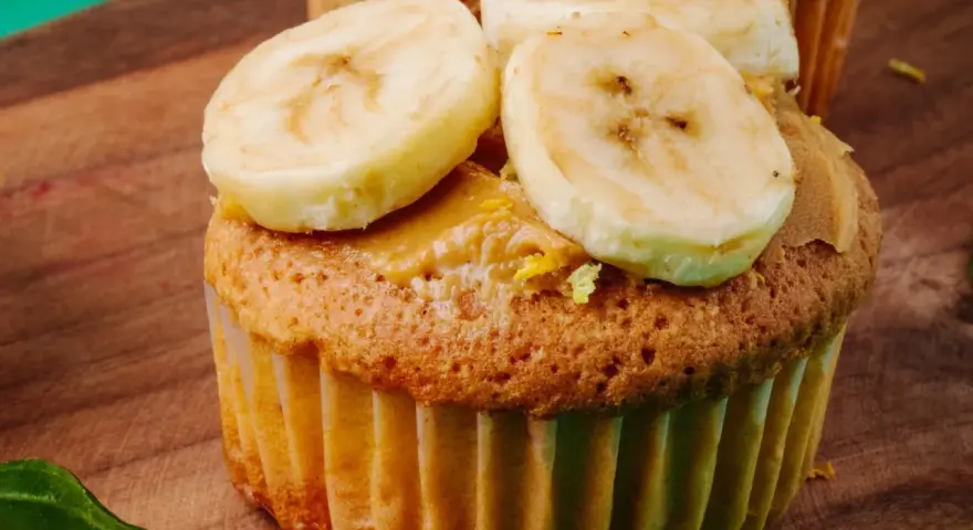 Pyszne muffinki bananowe z kremem orzechowym i plasterkami banana na drewnianej desce.