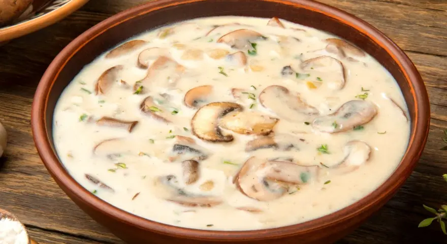 Aksamitna zupa pieczarkowa w glinianej misce, pełna kawałków pieczarek i ziół, na drewnianym stole.