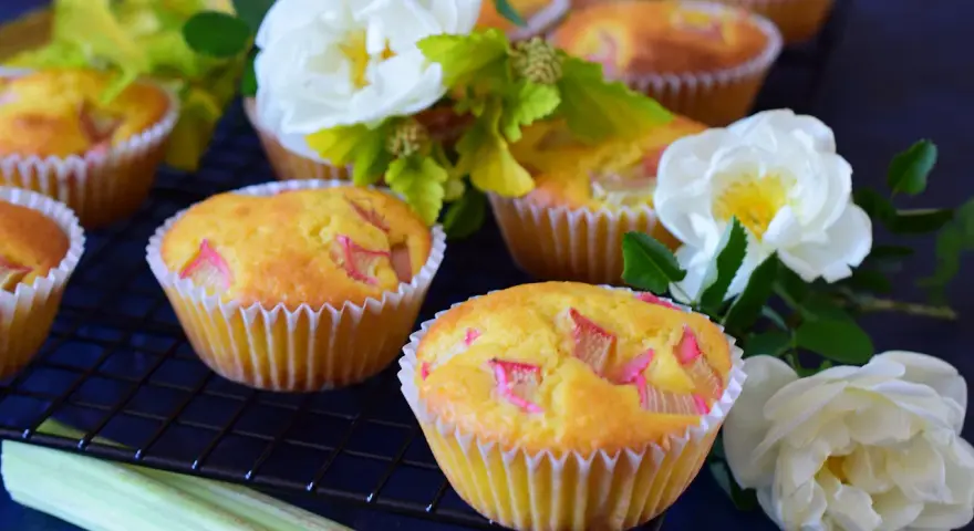 Pyszne muffinki z rabarbarem, ozdobione białymi różami i zielonymi liśćmi, kuszą swoim wyglądem.