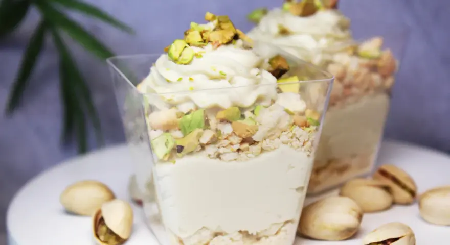 Pyszny deser w pucharku z kremową masą pistacjową, posypany kawałkami pistacji i okruszkami.